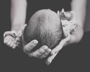 Black and white image of tiny newborn baby's head cradled in adult hands.
