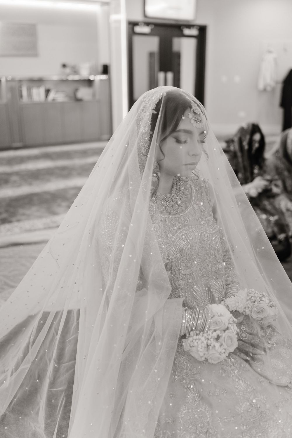Black and white portrait of South Asian bride in heavily embroidered lehenga with sparkle dupatta.