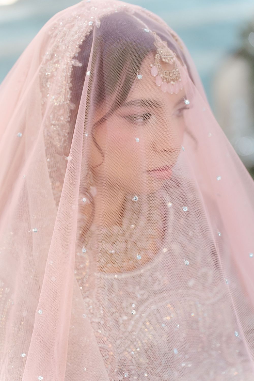 South Asian bride draped in pink sequined dupatta with gold maang tikka in soft dreamy light.