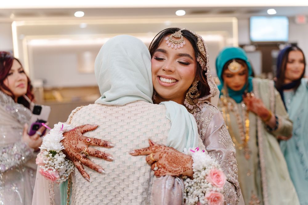 South Asian bride with mehndi hands embracing guest while smiling at nikah wedding celebration.