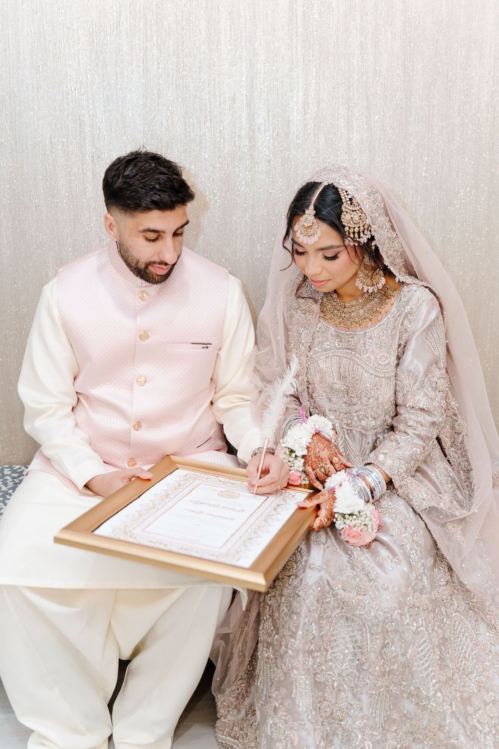 South Asian bride and groom sign their nikah marriage certificate in elegant traditional wedding outfits.