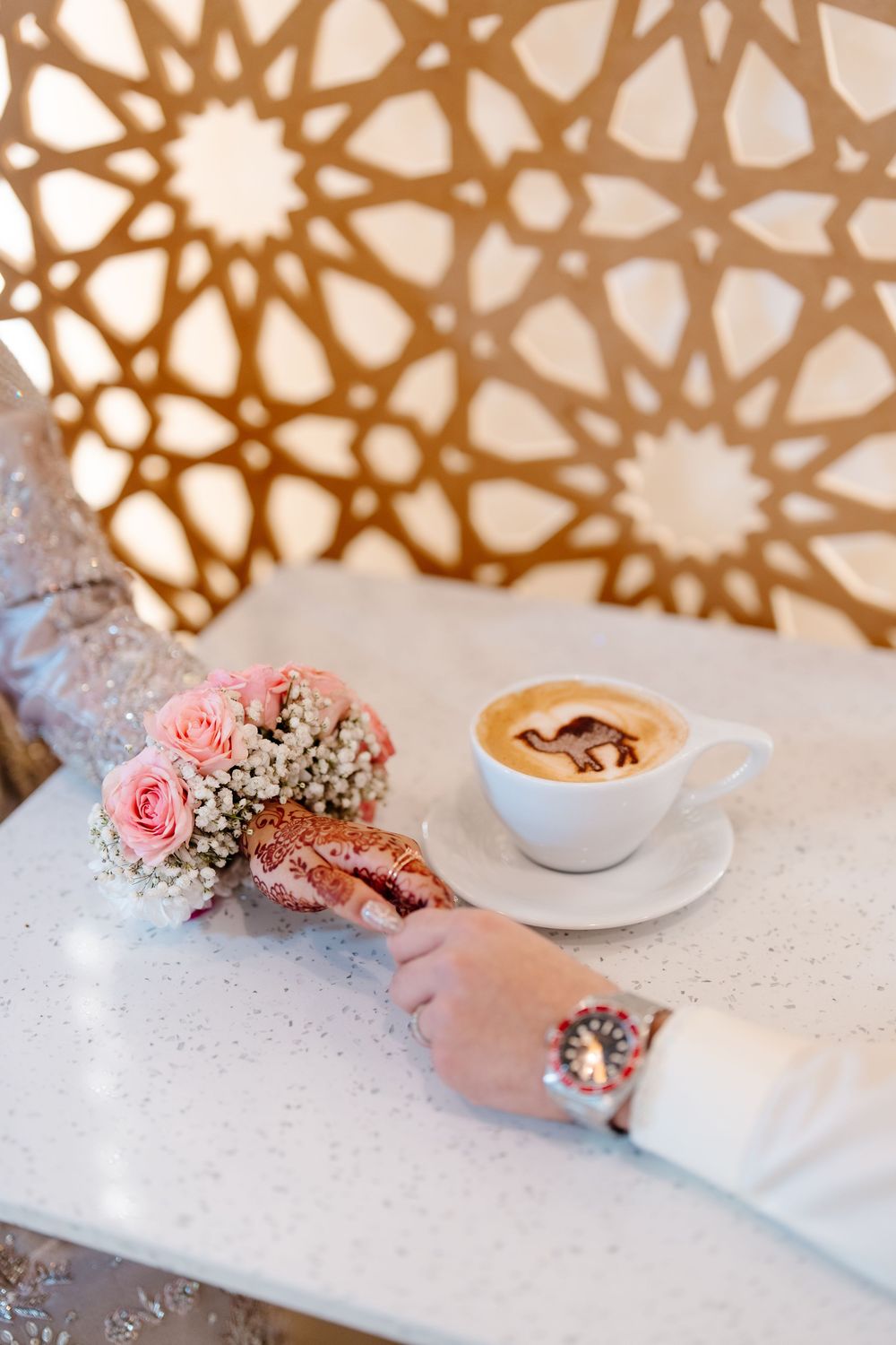 Bridal bouquet of pink roses beside a latte art coffee cup on a white table at a wedding.