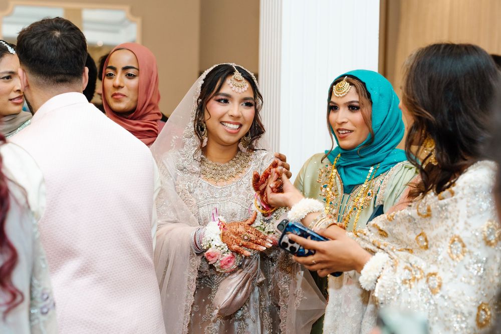 South Asian bride in embroidered gray lehenga smiles warmly while greeting guests at her wedding reception.