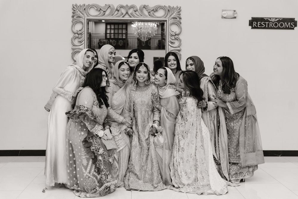 Black and white photo of a South Asian bride posing with her bridesmaids in traditional attire.