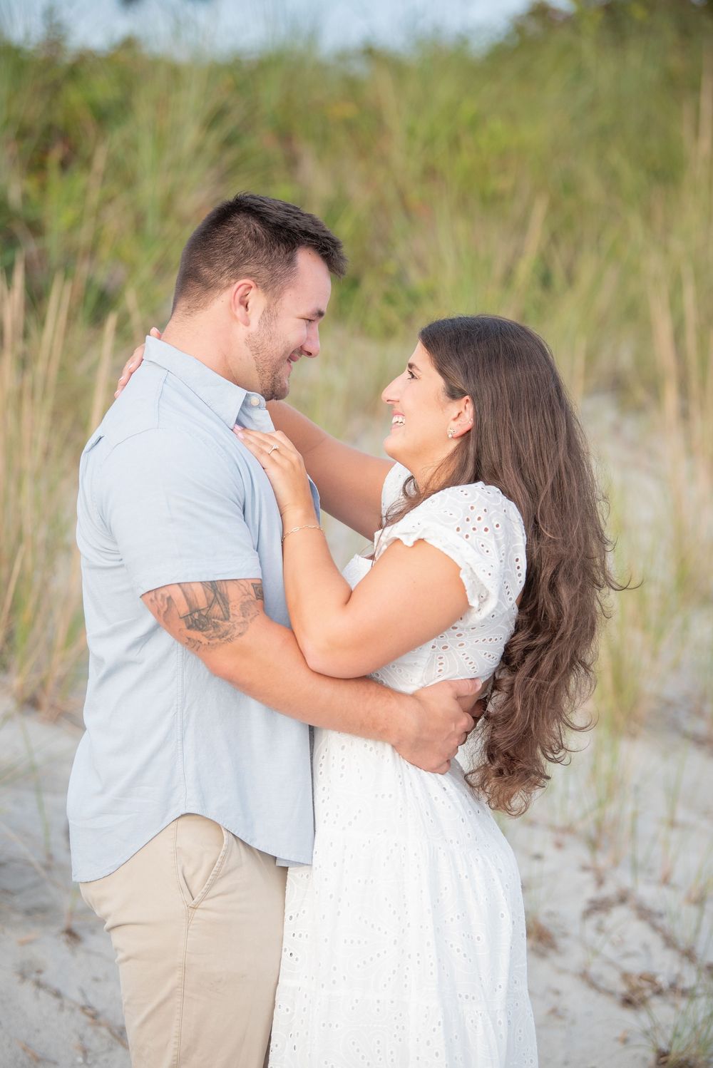 A couple laughs together during their beach photoshoot with dunes in the background.