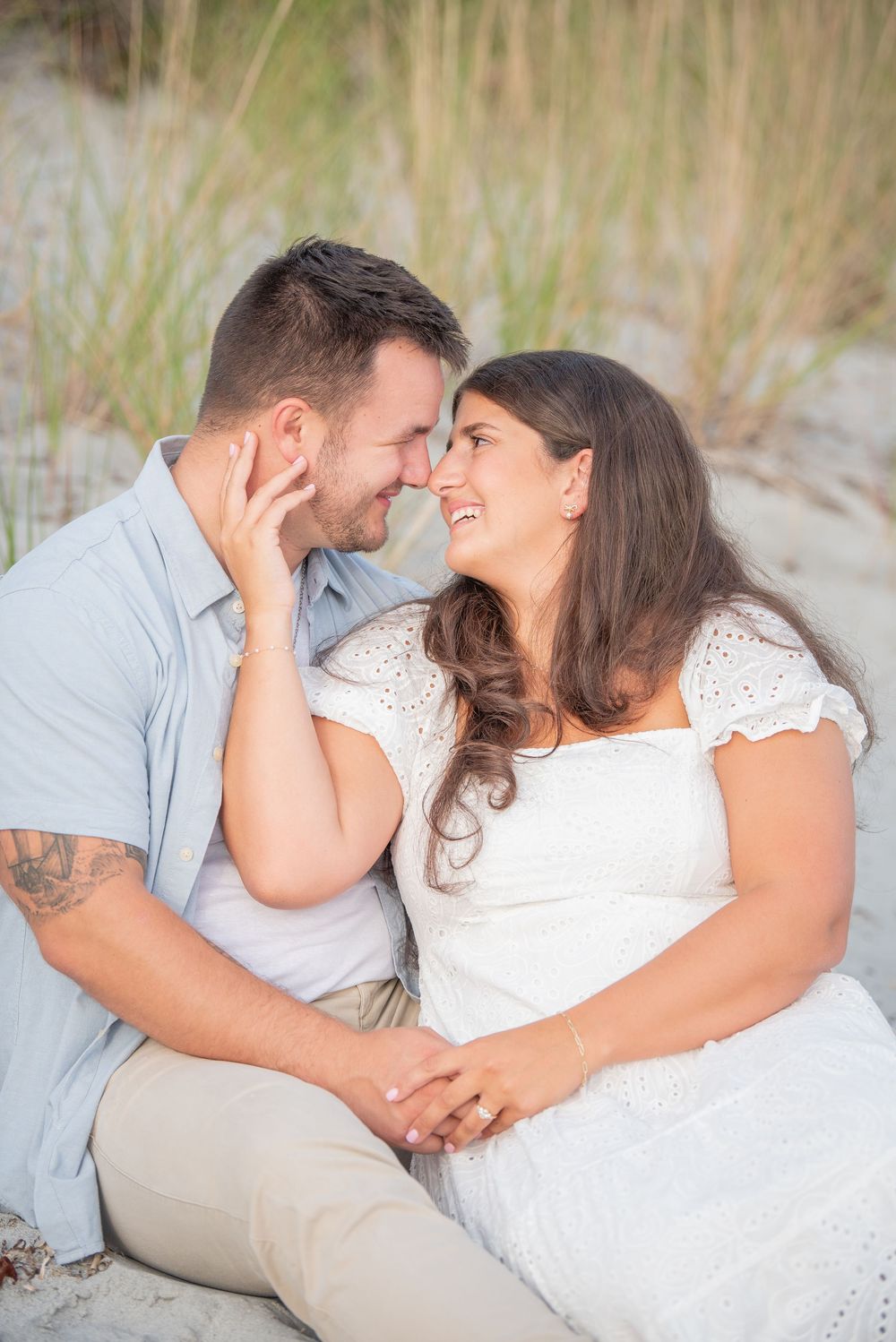 A couple shares a tender moment while sitting on the beach during their engagement session.