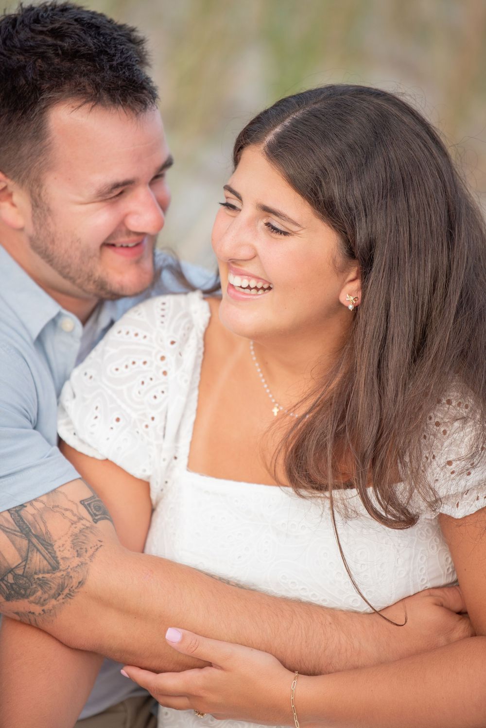 A couple shares an intimate moment of laughter while embracing on the beach.