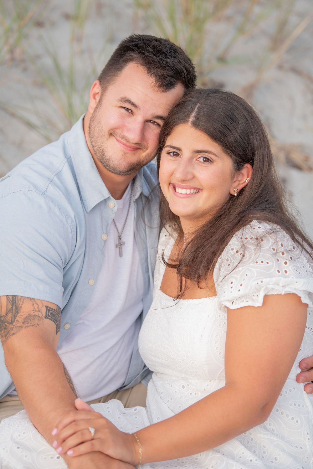 A loving couple poses for a portrait on the beach with dunes in the background.