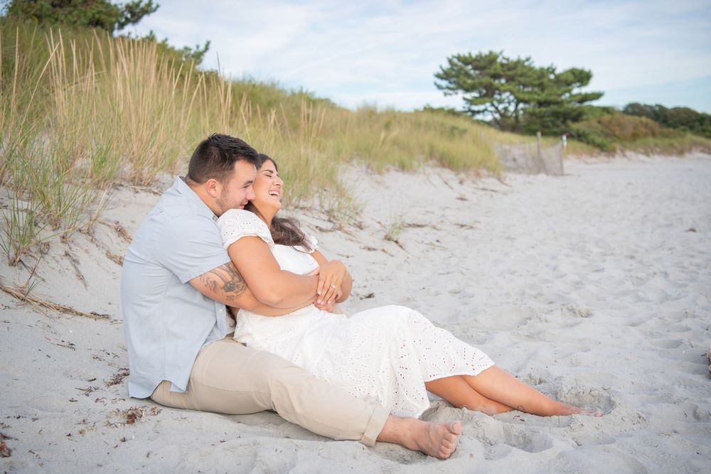 A romantic couple relaxes together on sandy beach dunes during a photo session.