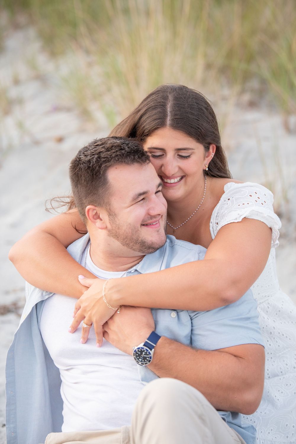 A couple shares a tender embrace while sitting on the beach during sunset.