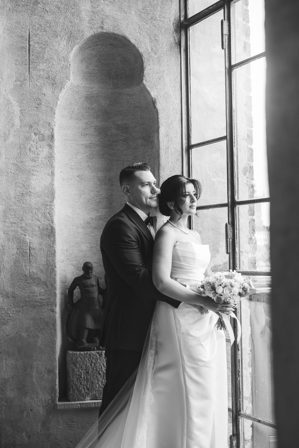A black and white wedding photograph series showing intimate moments between newlyweds by a window.
