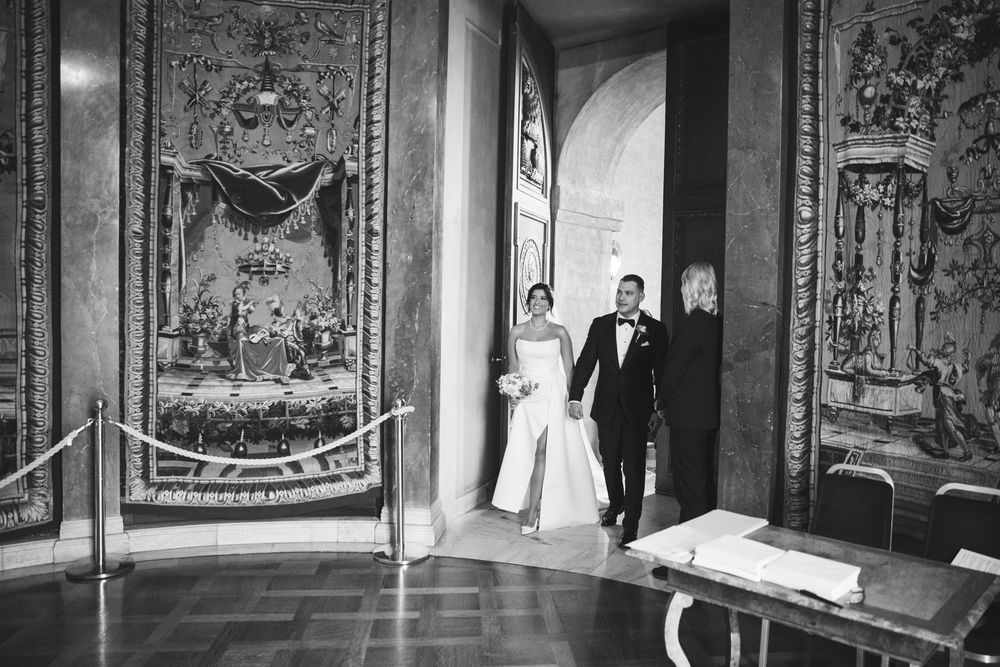Black and white photo of an elegant hallway with ornate tapestries and artwork lining the walls.