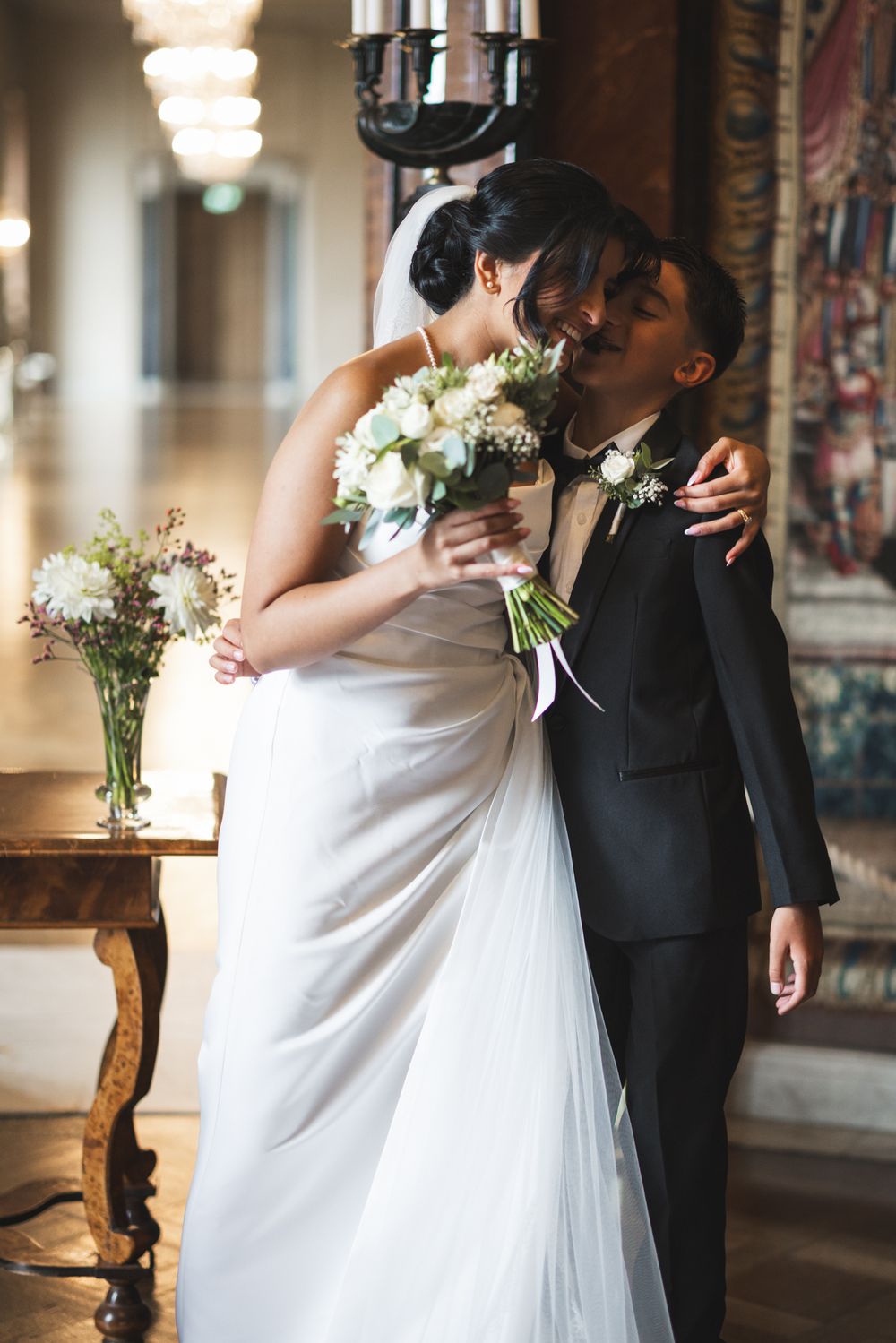 A bride in a white gown and groom in black tuxedo share a romantic kiss while holding a bouquet of white flowers.