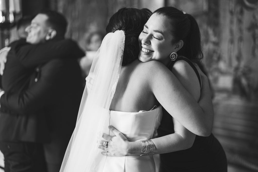Two people share an emotional embrace at a wedding celebration, captured in black and white photography.