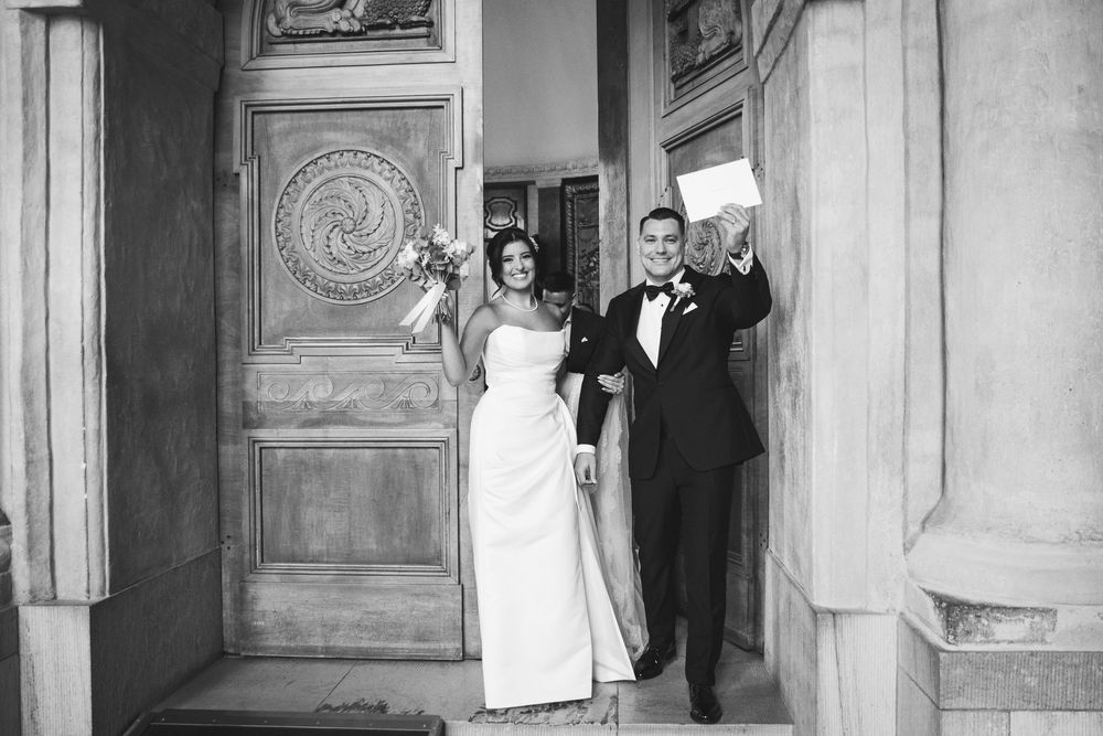 Black and white wedding photo showing a couple standing in an elegant doorway with ornate architectural details.