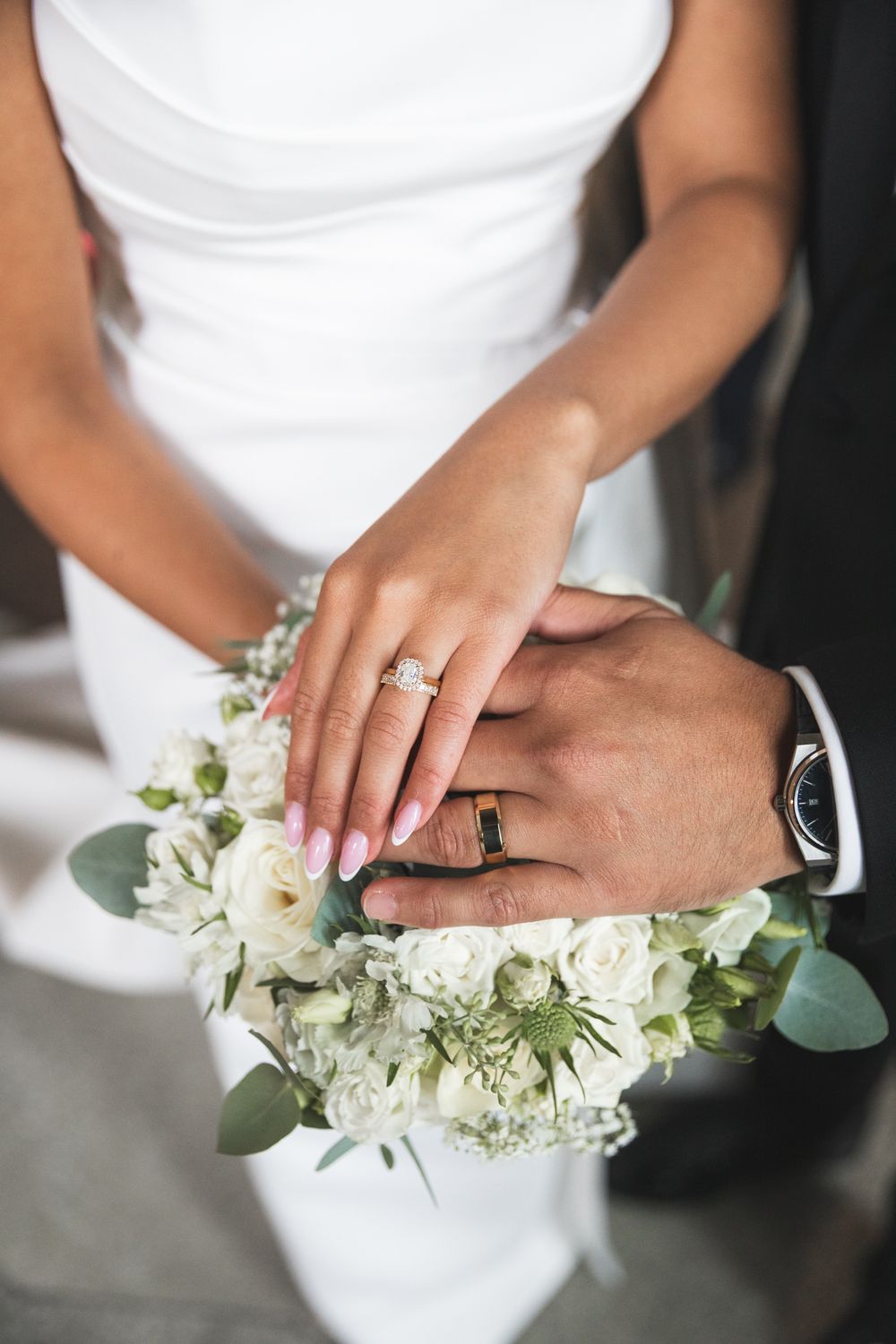 Close-up of hands with engagement ring holding delicate white floral bouquet with eucalyptus leaves.