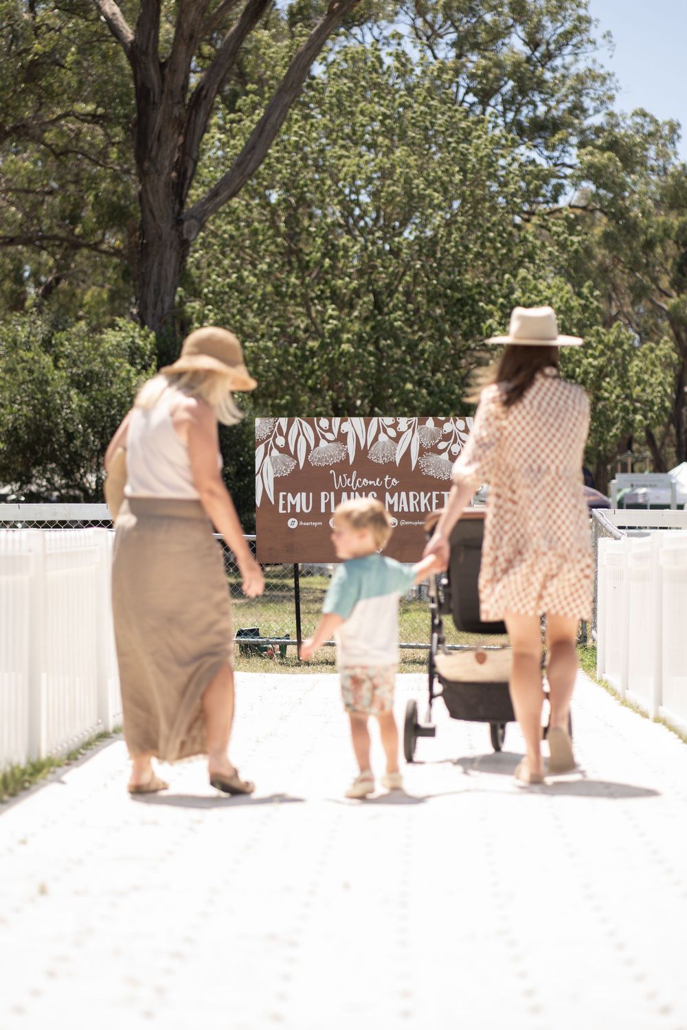 People walking along a white pathway at an outdoor market on a sunny day.