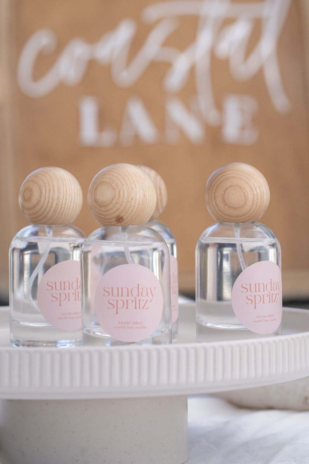 Three glass bottles with wooden caps labeled 'Sunday Spritz' displayed on a white shelf.