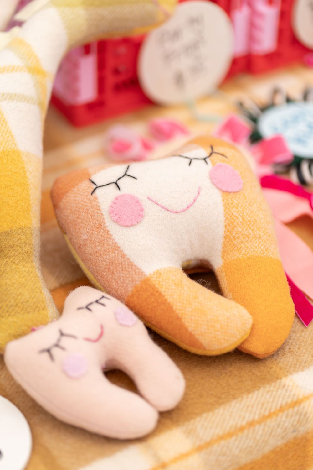 Adorable plush tooth-shaped pillows with sleepy faces and rosy cheeks on yellow fabric.