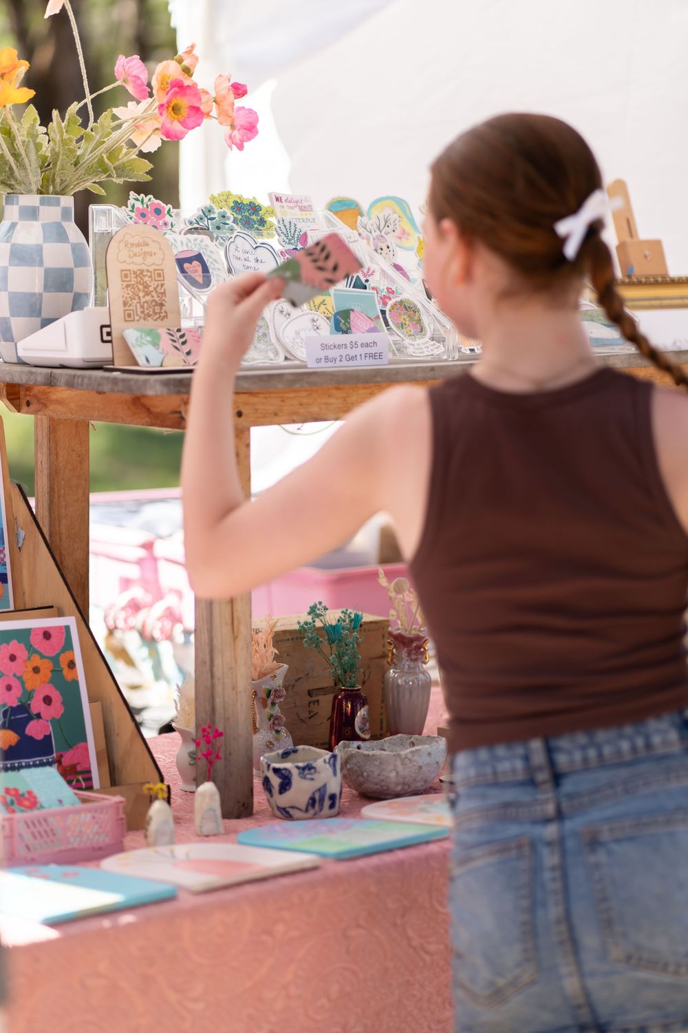 Customer browsing handmade items at an artistic market display with flowers.