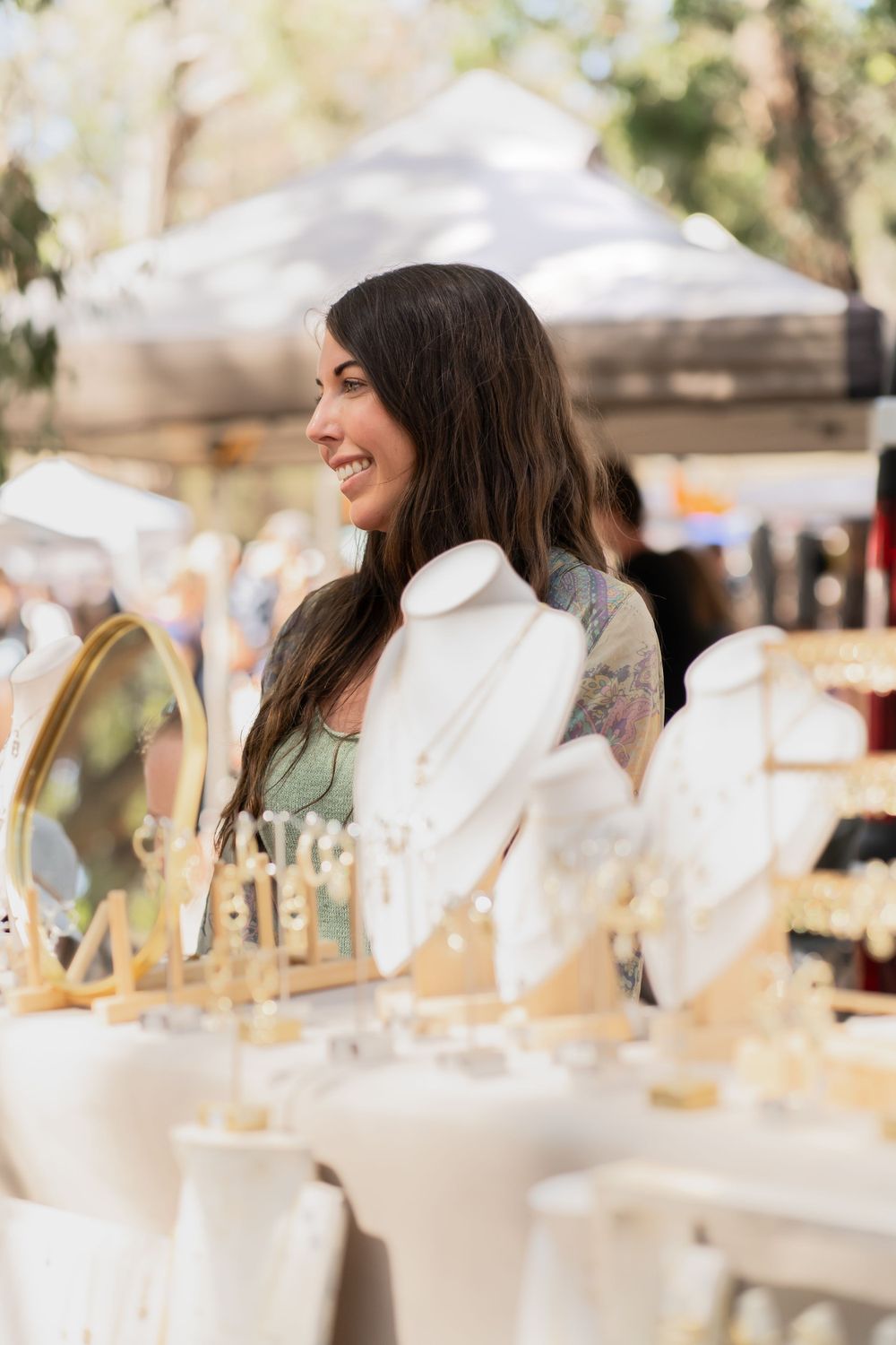 Artisan vendor smiling at an outdoor market display with white candles and decor.
