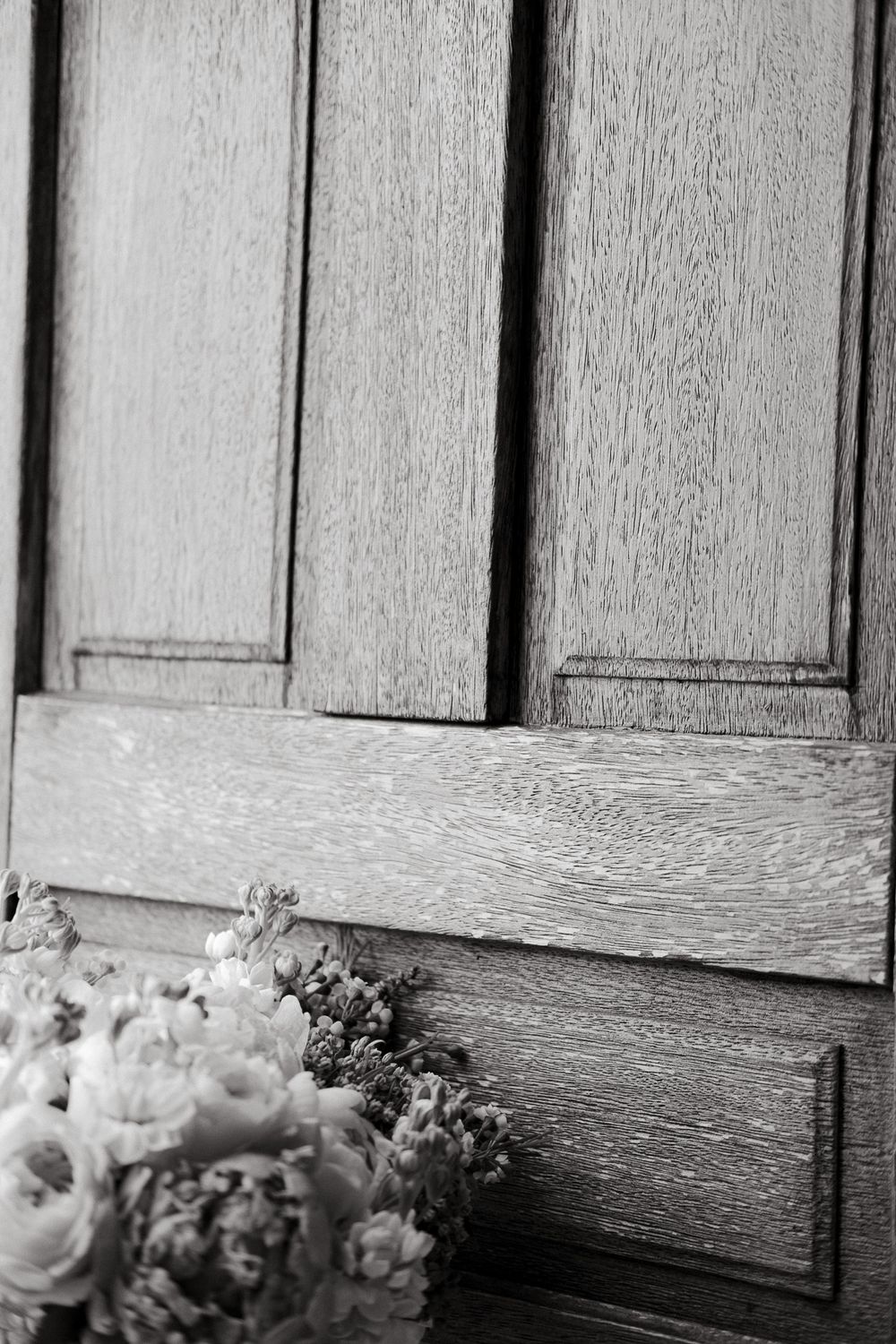 Wedding bouquet resting against a wooden door panel in black and white.