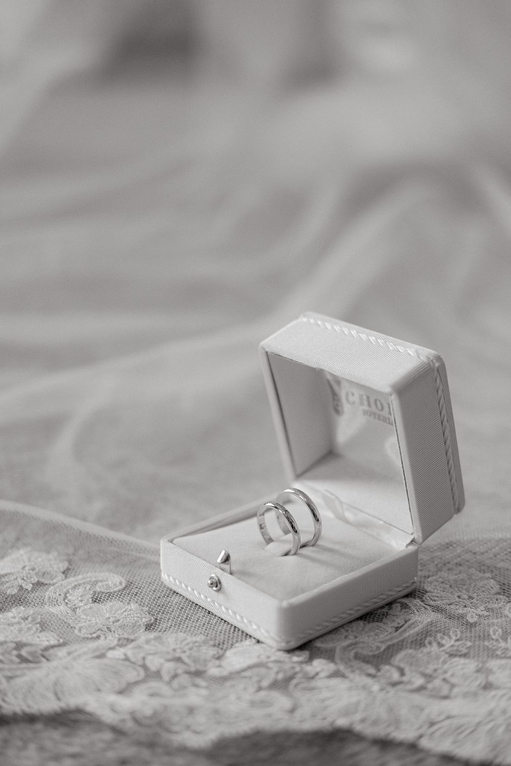 Wedding rings nestled in a white leather ring box on lace fabric.