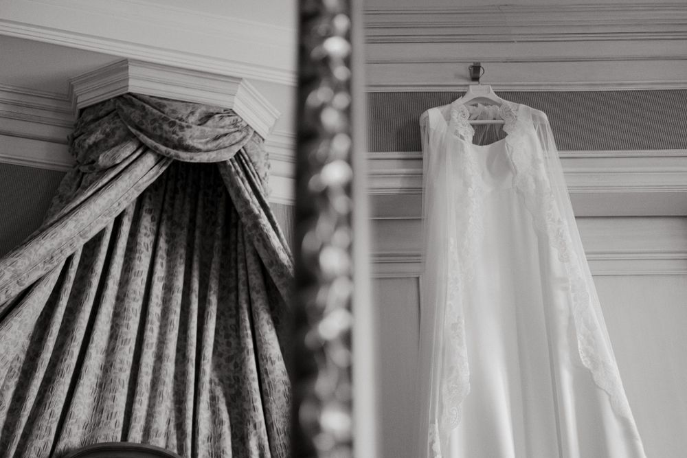 A wedding dress and ornate canopy hanging in a monochrome interior setting.