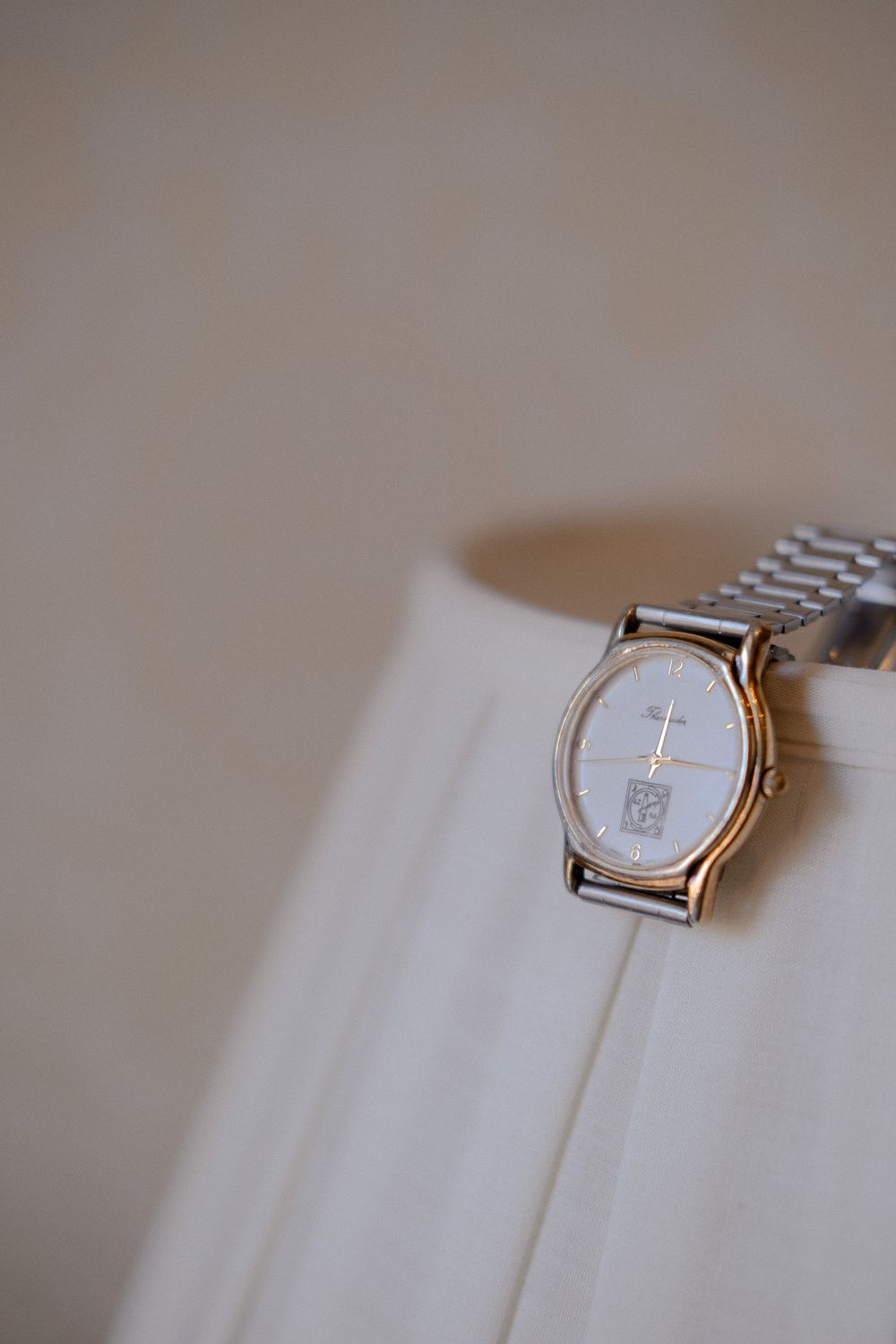 A silver wristwatch resting on white fabric with soft focus background.