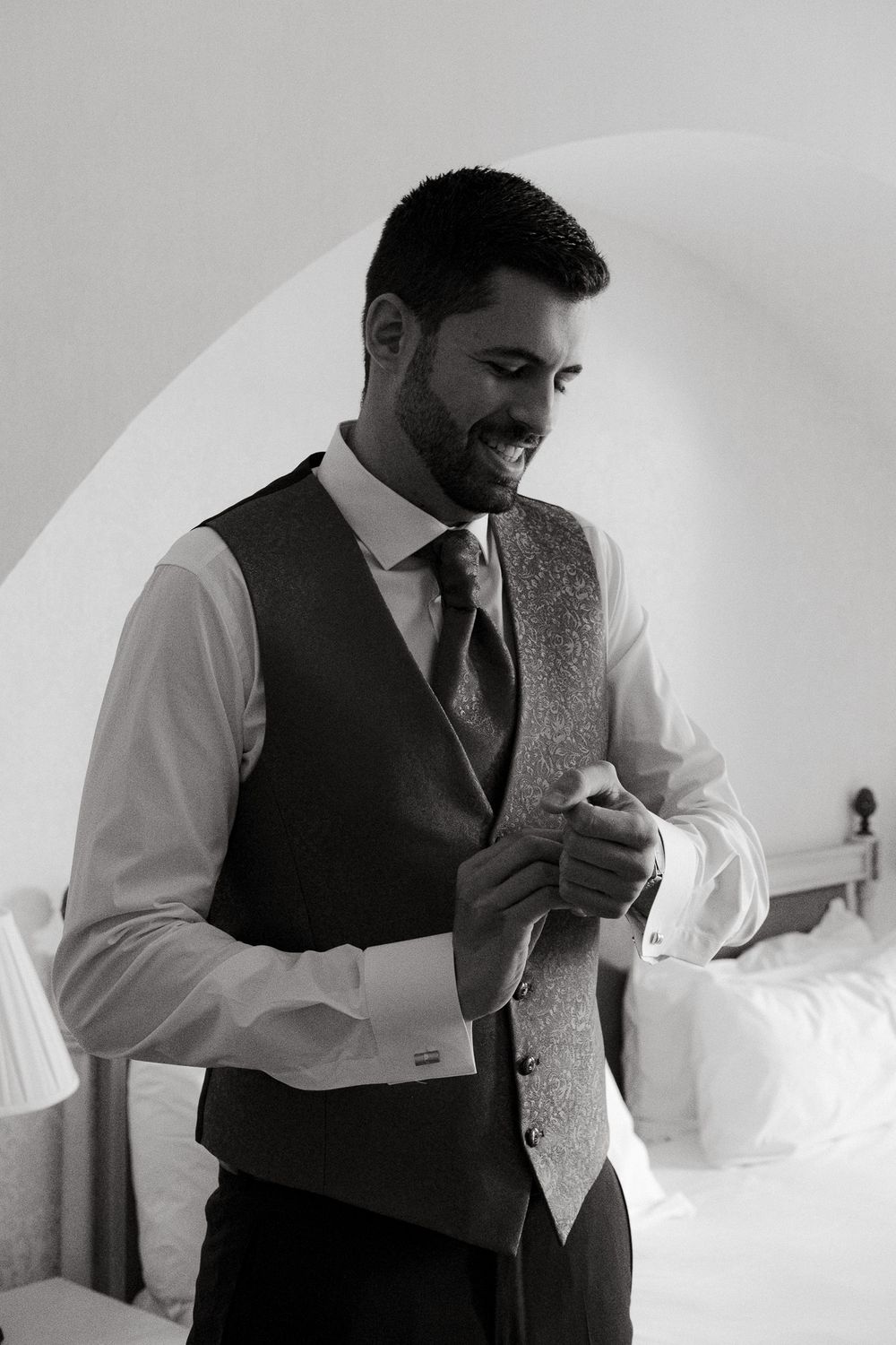 A person in formal attire adjusting their tie while getting dressed.