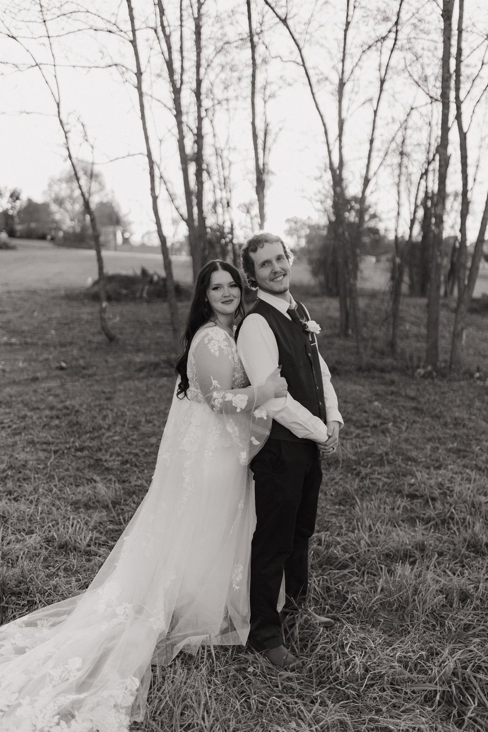 A black and white wedding portrait of a couple posing back-to-back outdoors.