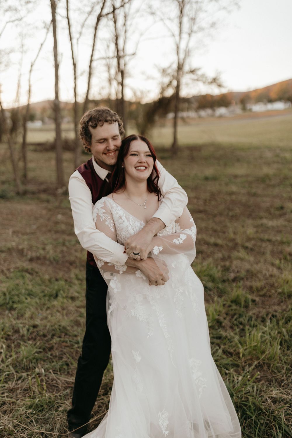 A joyful wedding couple embracing and laughing in a natural outdoor setting.