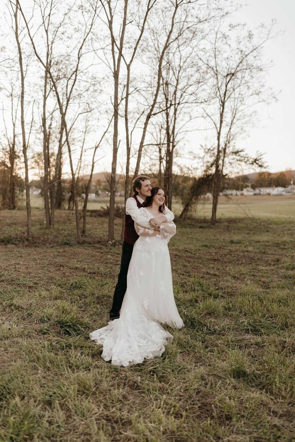 A romantic wedding photo of a couple embracing in a serene outdoor setting with bare trees.