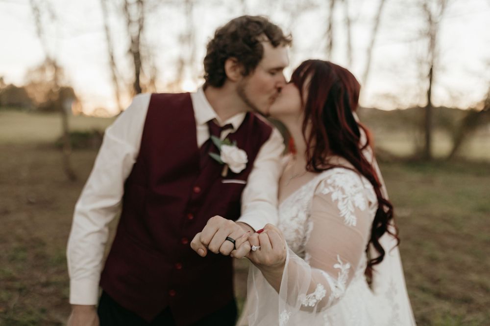 An intimate moment between newlyweds sharing a kiss while holding hands at sunset.
