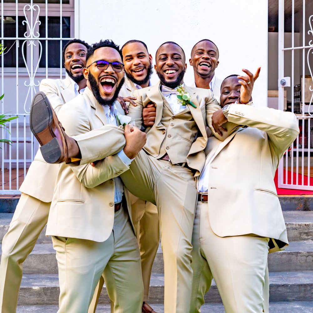 Groomsmen in cream colored suits celebrating joyfully on outdoor steps.