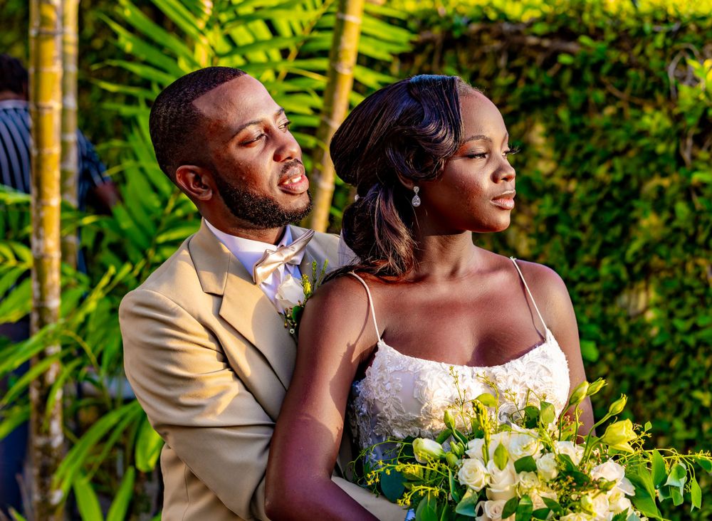 Couple in wedding attire pose together in tropical garden setting with yellow bouquet.