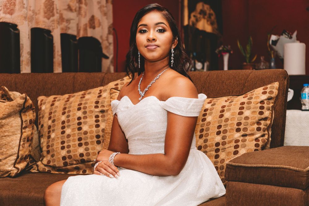 Elegant portrait in white off-shoulder dress seated on patterned cushions.