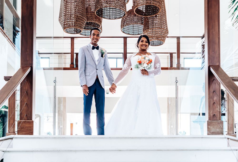 Wedding couple holding hands on white modern staircase under woven pendant lights.