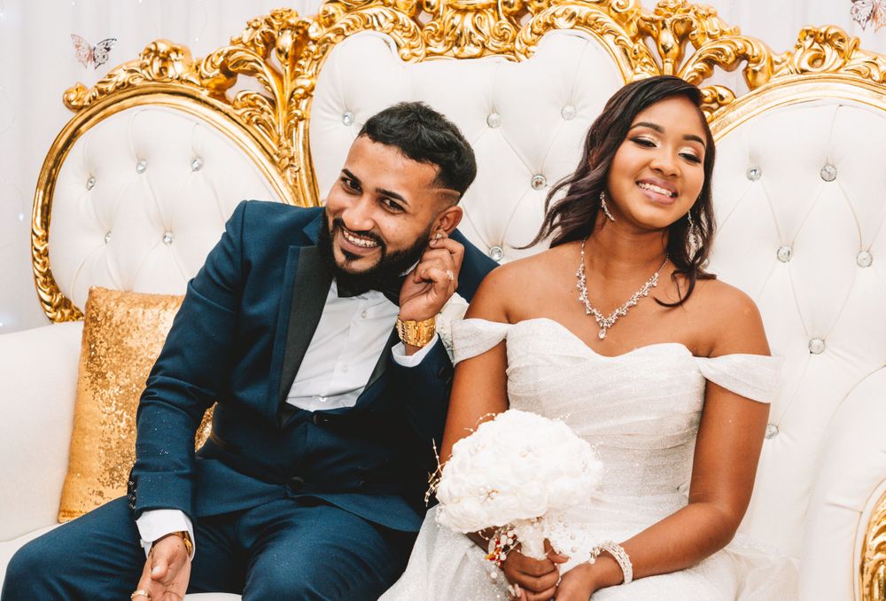 A couple sits on an ornate gold and white sofa during their wedding celebration.