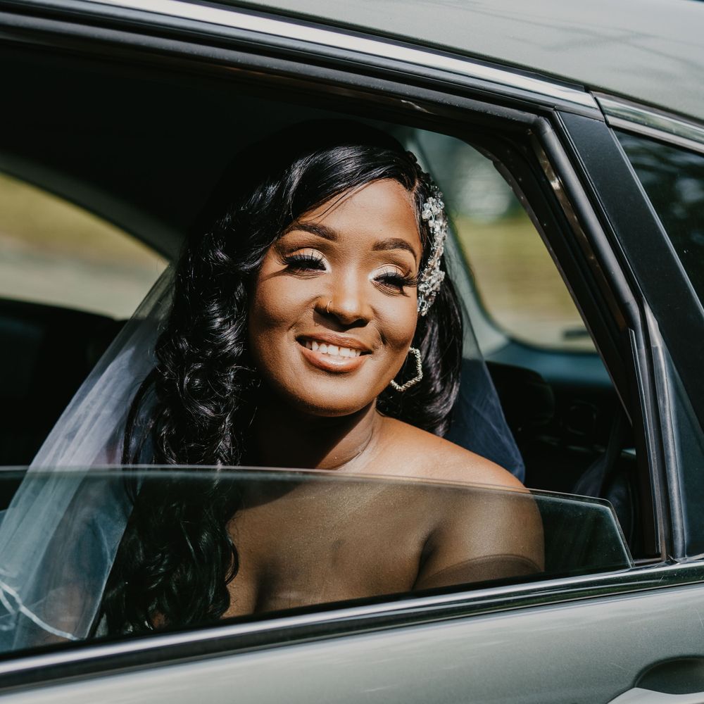A bride smiles radiantly from inside a car window on her wedding day.