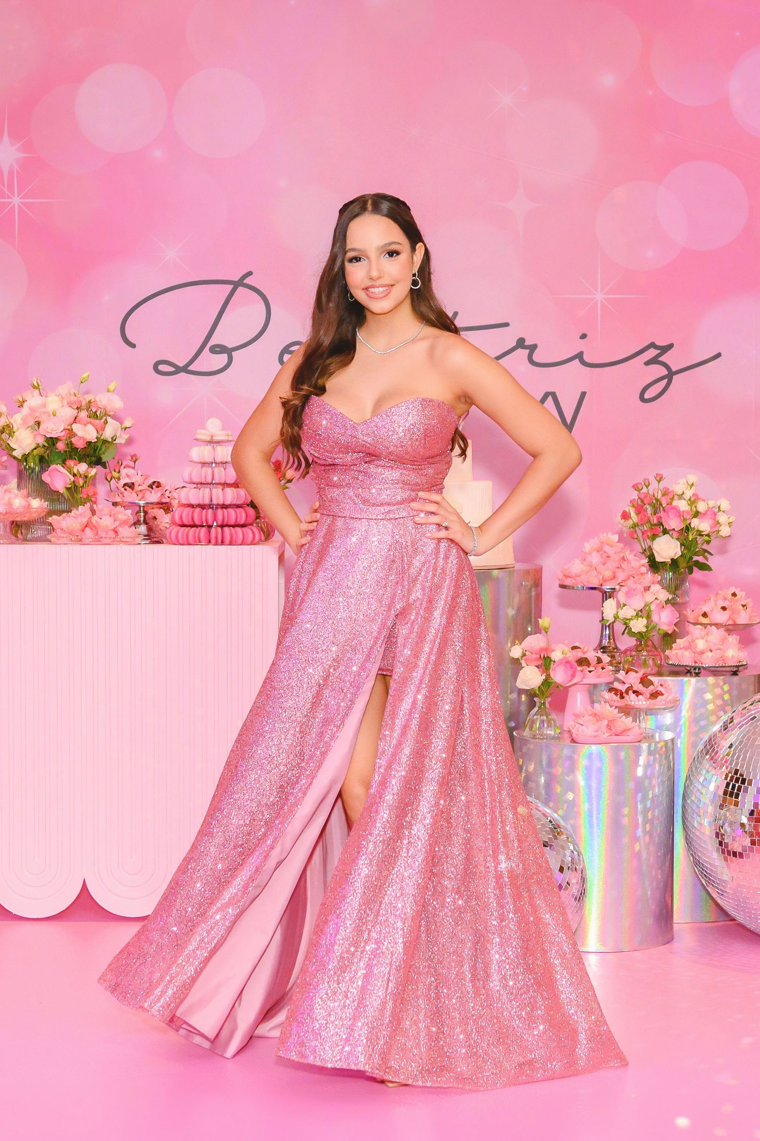 Party decor features blue and gold balloons with floral arrangements surrounding a person in a sparkly blue strapless dress.