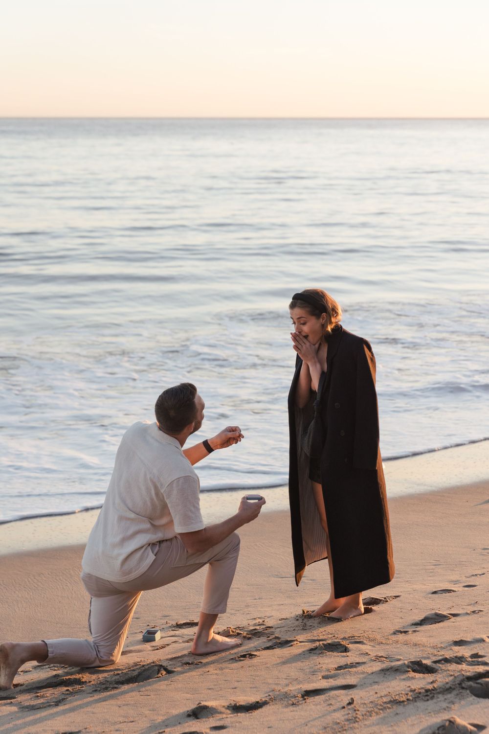 A romantic beach proposal scene during sunset with waves in the background.