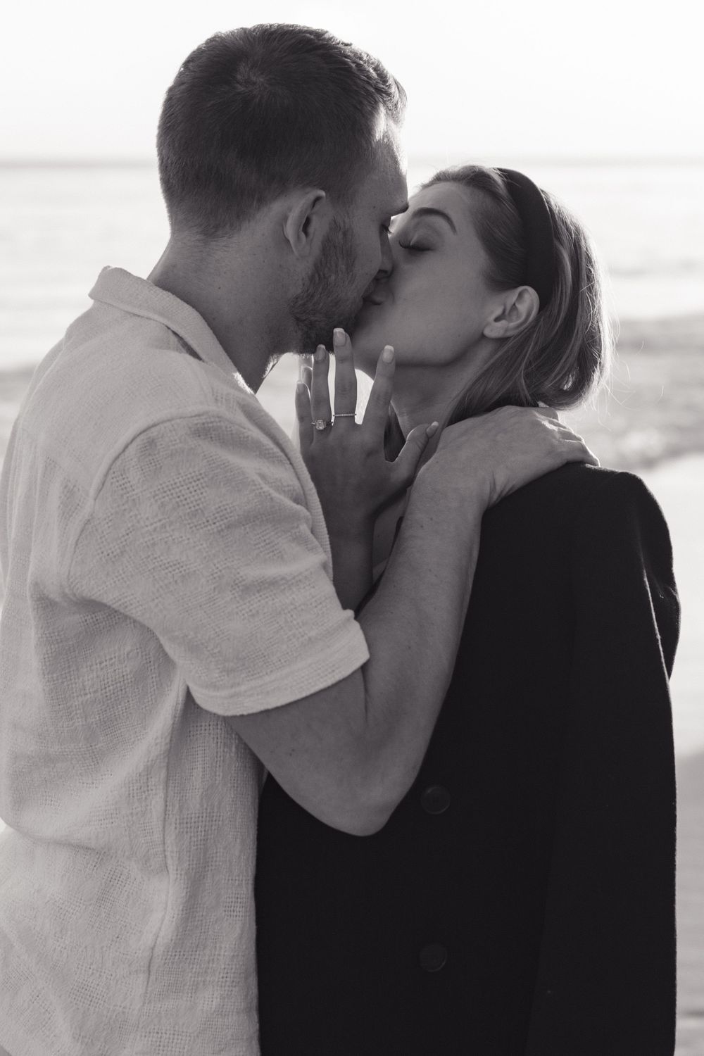 A romantic couple shares a passionate kiss on the beach in black and white photography.