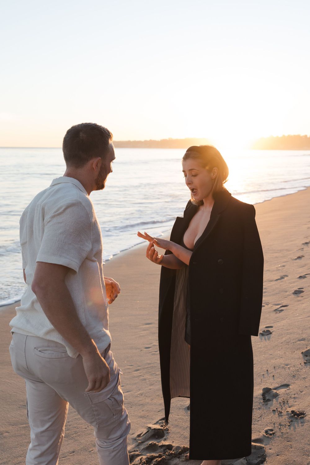 A couple having a discussion on a beach at sunset, with one person wearing all white and the other in dark clothing.