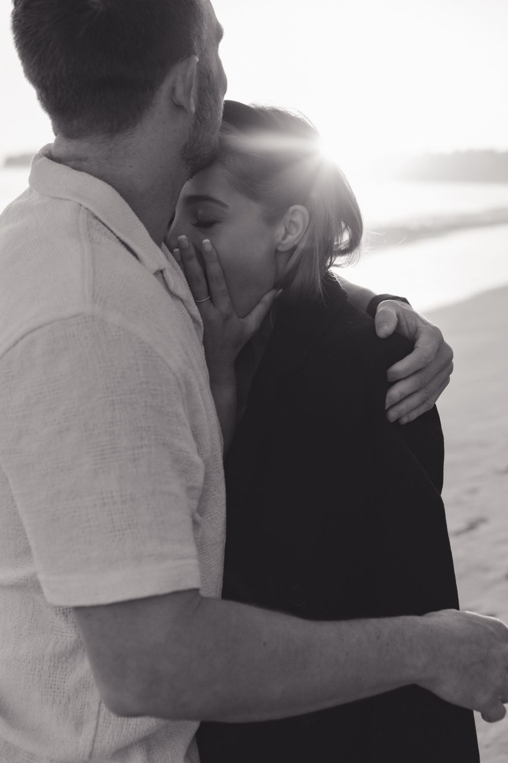 Romantic black and white photo of a couple embracing on the beach at sunset.