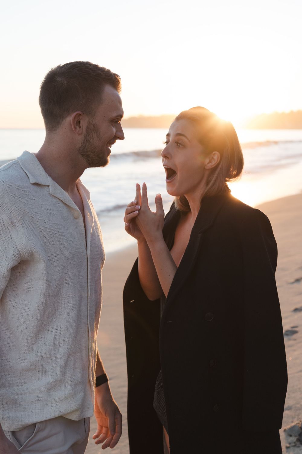 A joyful couple laughs together on the beach during golden hour sunset.