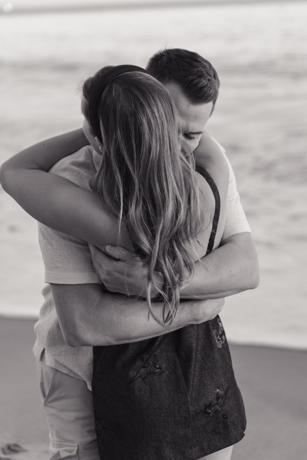 A romantic black and white beach embrace between a couple during a tender moment.