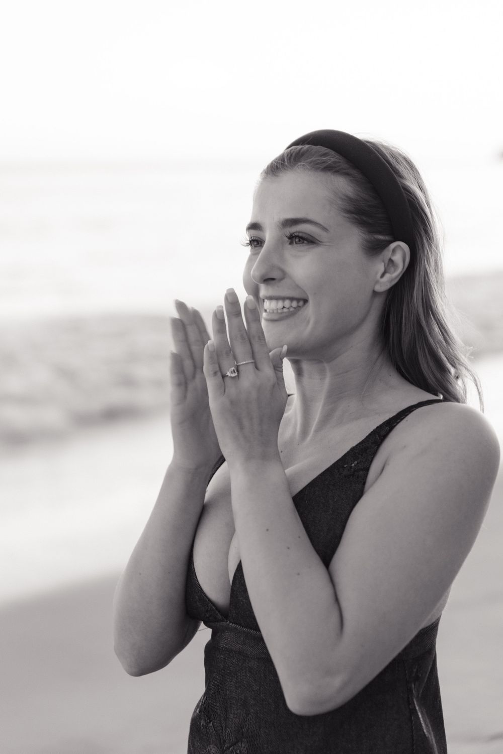 A joyful moment captured in black and white as someone shows off their engagement ring on the beach.