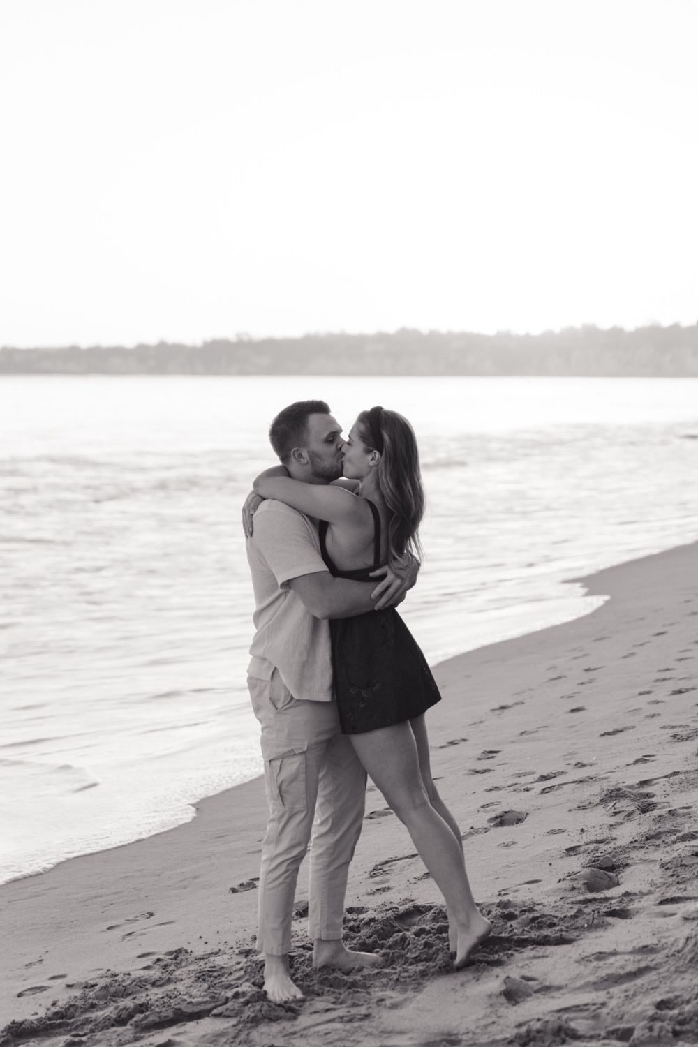 A couple embraces in a romantic black and white moment on the beach.