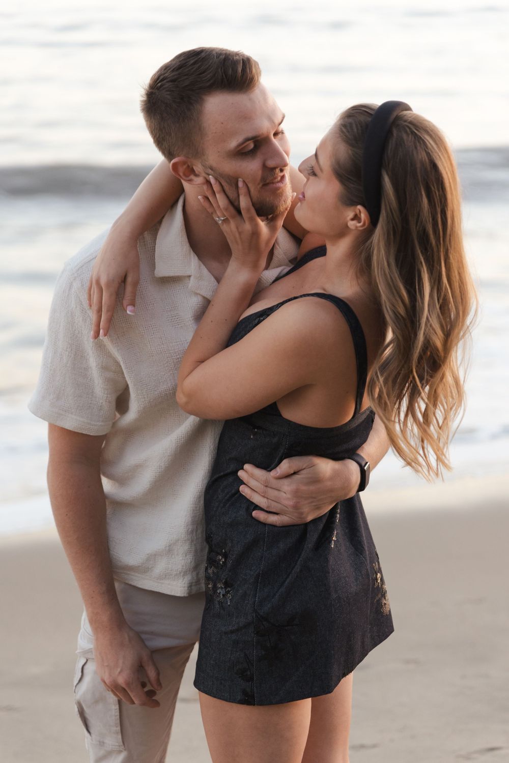 Romantic couple embracing on a beach during sunset, sharing an intimate moment by the ocean.